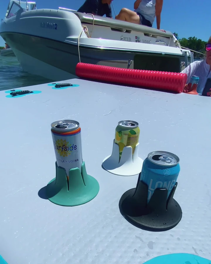 Three beverage cans in Steadi holders, with their full bases resting on the gray deck of a turquoise inflatable lake platform